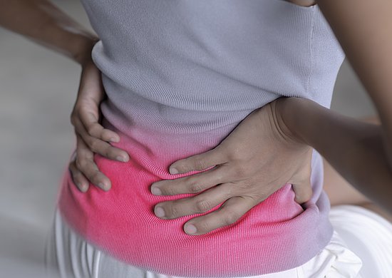 Eine Frau sitzt und hält sich die Hände an den Rücken. 