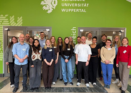 Das Bild zeigt die Teilnehmenden und Organisator*innen der Summer School. Die Gruppe steht vor dem Seminarbereich und im Hintergrund ist das Wappen der Universität Wuppertal zu erkennen. 