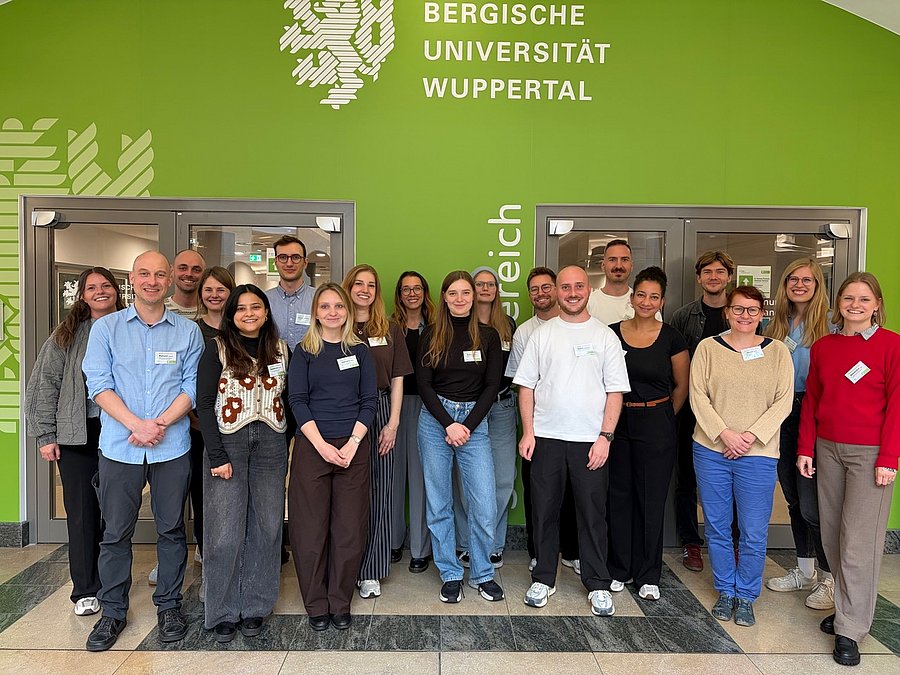 Das Bild zeigt die Teilnehmenden und Organisator*innen der Summer School. Die Gruppe steht vor dem Seminarbereich und im Hintergrund ist das Wappen der Universität Wuppertal zu erkennen. 