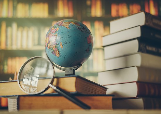 Zu sehen ist ein Globus vor einem Bücherregal. Eine Lupe liegt daneben
