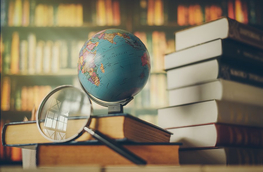 Zu sehen ist ein Globus vor einem Bücherregal. Eine Lupe liegt daneben