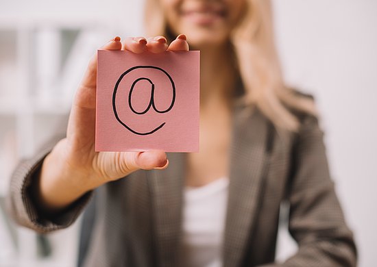 Eine Frau hält ein Post-It mit einem großen @Zeichen