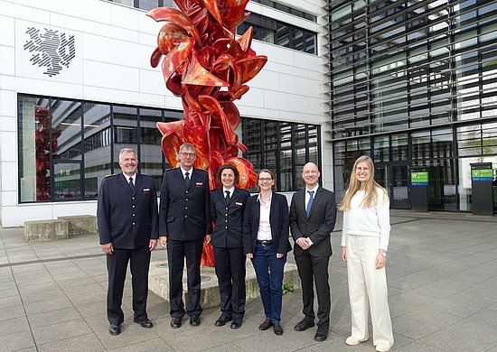 Das Projektteam nach der Vertragsunterzeichnung: (v.l.) Dr. Hauke Speth (IdF NRW), Berthold Penkert (IdF NRW), Sarah Weber (IdF NRW); Uni-Kanzlerin Dr. Ursula Löffler (BUW), Prof. Dr. Meinald Thielsch (BUW) und Dr. Mira von der Linde (BUW). Alle stehen vor einer Statue am Campus Grifflenberg